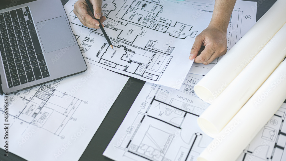 Architectural building design and construction plans with blueprints, Young man was designing a building or architecture with a ruler, pen, pencil, tape measure, architect hat and other equipment. - obrazy, fototapety, plakaty 