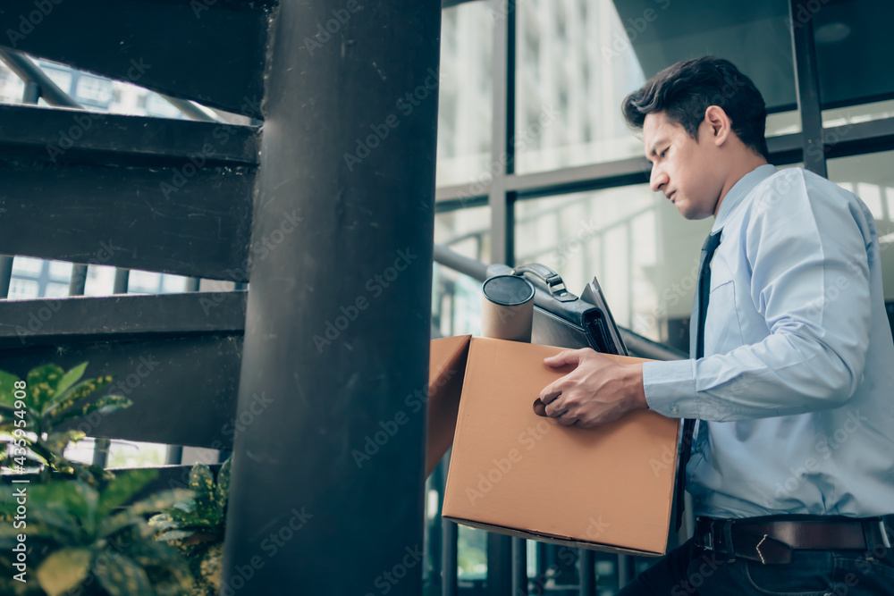 Unemployed hold cardboard box and laptop bag, dossier and drawing tube in box. Quiting a job, businessman fired or leave a job concpet.