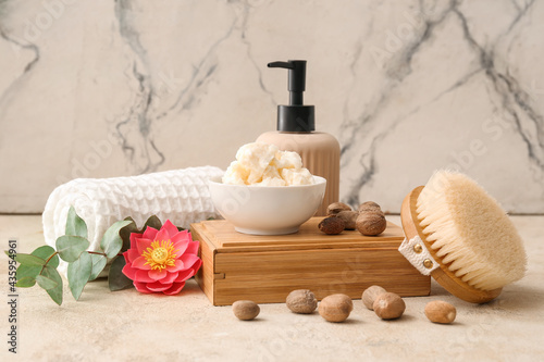 Bowl with shea butter, nuts and bath supplies on light background