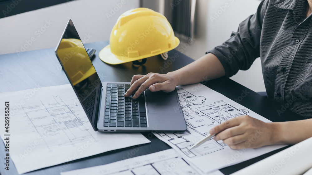 Young man with a laptop plotting a system of building structures in blueprints, Architects or engineers are designing buildings using computers to calculate the physical structure to be correct. Young man with a laptop plotting a system of building structures in blueprints, Architects or engineers are designing buildings using computers to calculate the physical structure to be correct.