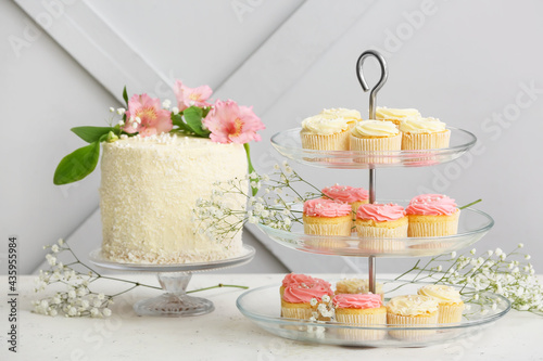 Dessert stands with tasty cupcakes, cake and flowers on table