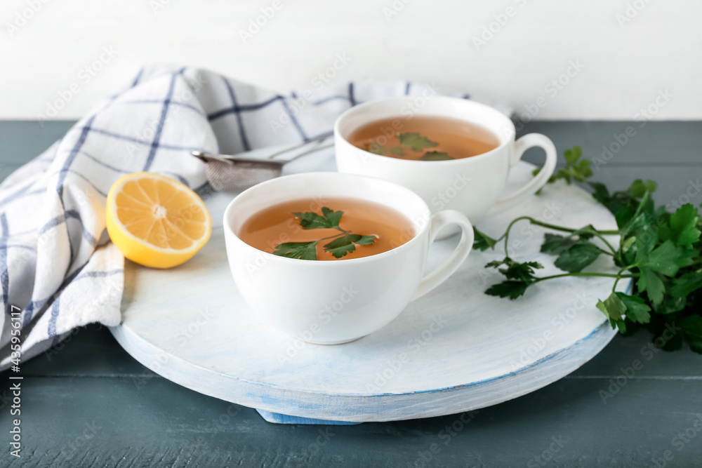 Board with cups of hot tea, parsley and lemon on color wooden background Board with cups of hot tea, parsley and lemon on color wooden background