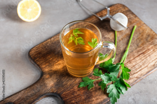 Board with cup of hot tea, parsley and lemon on grunge background