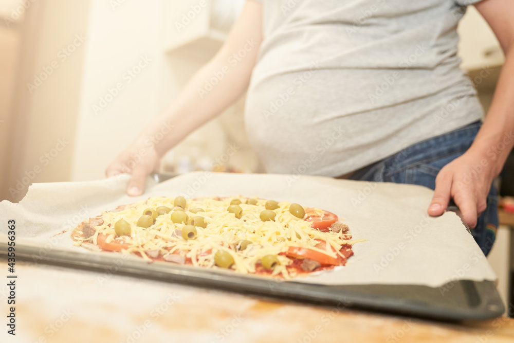 Pregnant woman holds on a baking sheet prepared for baking healthy gluten-free pizza with beef. Gluten-free cooking class. Cooking at home. 