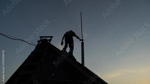 A male worker cleans a chimney on the roof at sunset in the late evening.Clean the soot in the chimney.Dioxides,harmful exhaust fumes,air and environmental pollution.Chimney and pipe cleaning service