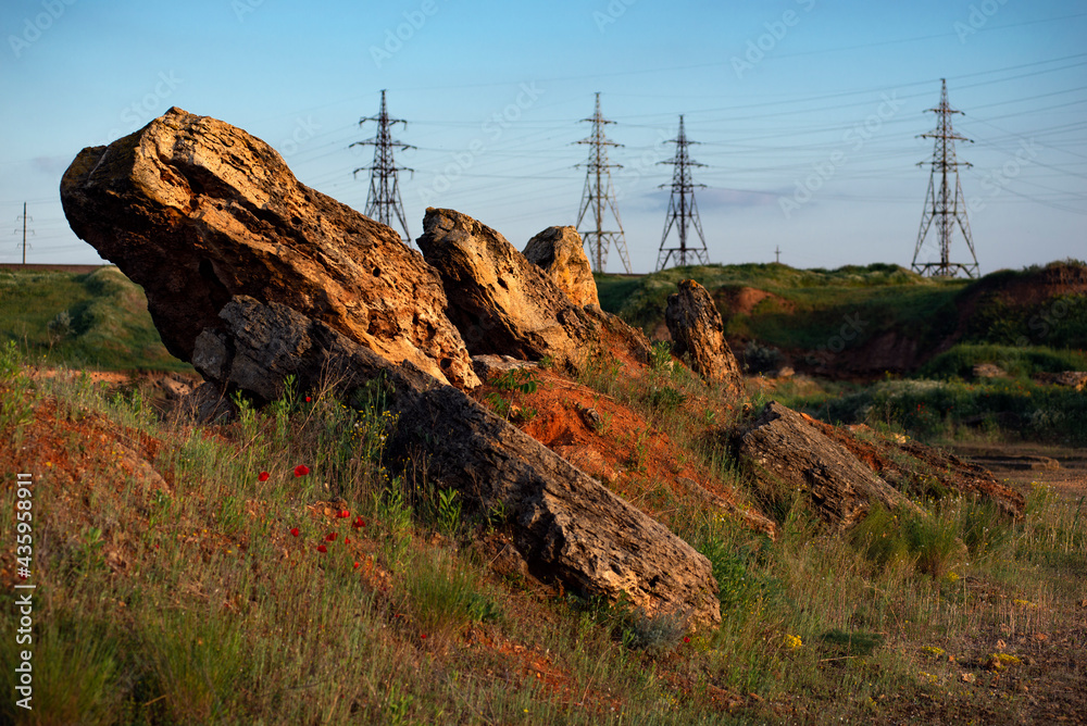 Stones in the foreground. Quarry and high-voltage towers.Powerful lines of electric gears.Electric power industry and nature concept.High voltage power lines.Field and aerial lines, silhouettes at dus