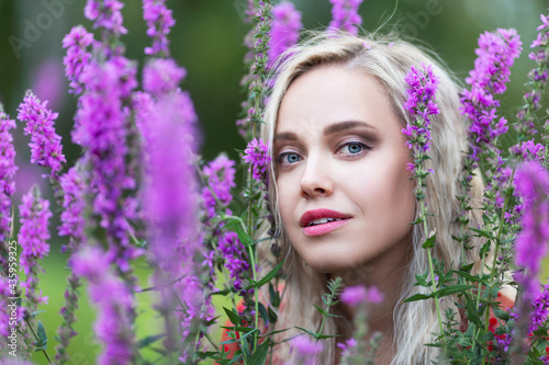 Young blonde girl in the bushes of purple flowers. Close-up.
