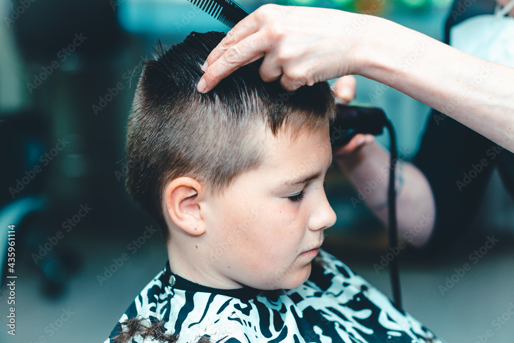 Fototapeta premium Cute kid have hair cut,professional barber doing haircut. Hairdress for children. side view portrait barbershop.Toned
