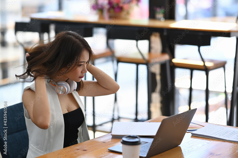 Young female wearing earphone and working with laptop while sitting cafe.