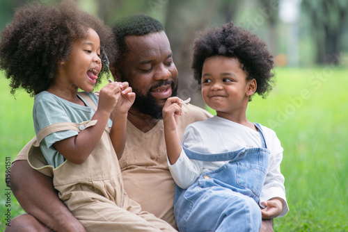 African father and daughter and son had a great time at the outdoor park, two children happily sitting on their father's lap, Father's day
