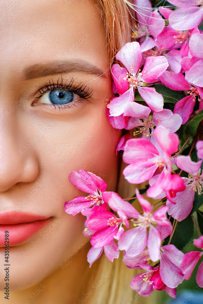 A large portrait of a woman with a pink cherry blossom flower near her face. A blonde with blue eyes enjoys the aroma of cherry blossoms in the spring. Beauty portrait A large portrait of a woman with a pink cherry blossom flower near her face. A blonde with blue eyes enjoys the aroma of cherry blossoms in the spring. Beauty portrait
