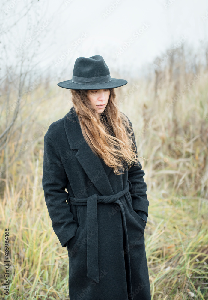Obraz premium Portrait of young attractive woman in black coat and hat.
