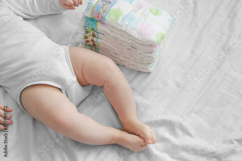 Baby feet and a pack of diapers on a white bed. Dirty diapers. Newborn and costs
