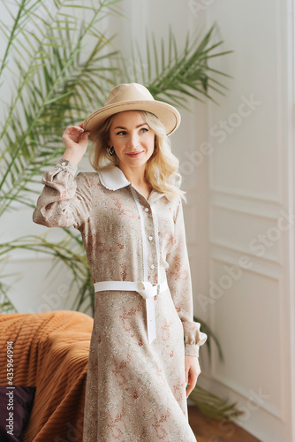 Luxurious young slim girl with long hair in a long dress with a floral print and a straw hat. Getting ready is going on a date on a warm summer evening