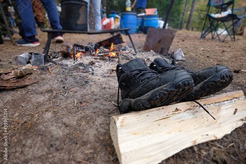 Camping. In the foreground, black shoes are dried, in the background fire.