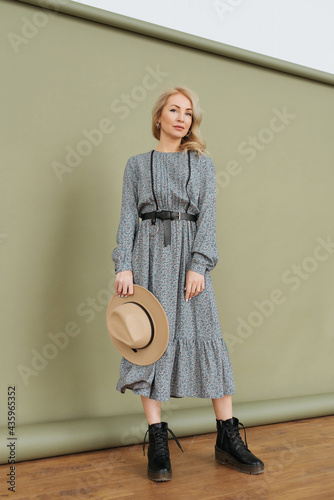 Luxurious young slim girl with long hair in a long dress with a floral print and a straw hat. Getting ready is going on a date on a warm summer evening