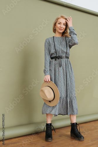 Luxurious young slim girl with long hair in a long dress with a floral print and a straw hat. Getting ready is going on a date on a warm summer evening
