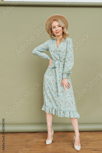 Luxurious young slim girl with long hair in a long dress with a floral print and a straw hat. Getting ready is going on a date on a warm summer evening
