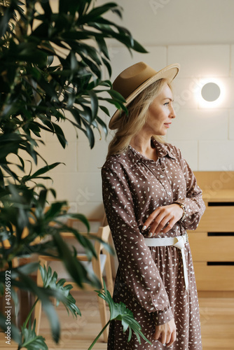 Luxurious young slim girl with long hair in a long dress with a floral print and a straw hat. Getting ready is going on a date on a warm summer evening