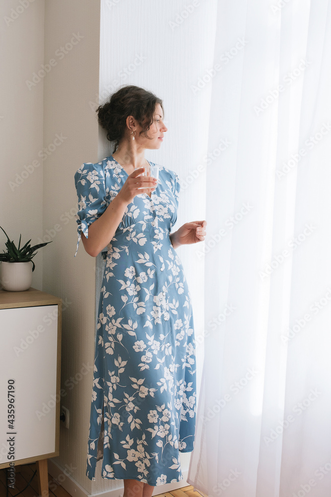 adult young woman is resting in a beautiful feminine blue dress in a bright room by the window relax rest break anticipation anticipation date adult young woman is resting in a beautiful feminine blue dress in a bright room by the window relax rest break anticipation anticipation date