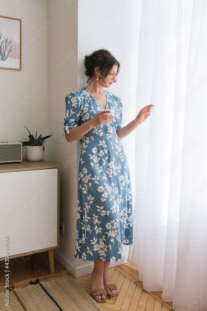 adult young woman is resting in a beautiful feminine blue dress in a bright room by the window relax rest break anticipation anticipation date adult young woman is resting in a beautiful feminine blue dress in a bright room by the window relax rest break anticipation anticipation date