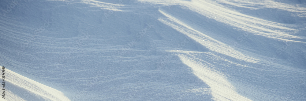 Beautiful winter background with snowy ground. Natural snow texture. Wind sculpted patterns on snow surface. Wide panoramic texture for background and design. Beautiful winter background with snowy ground. Natural snow texture. Wind sculpted patterns on snow surface. Wide panoramic texture for background and design.