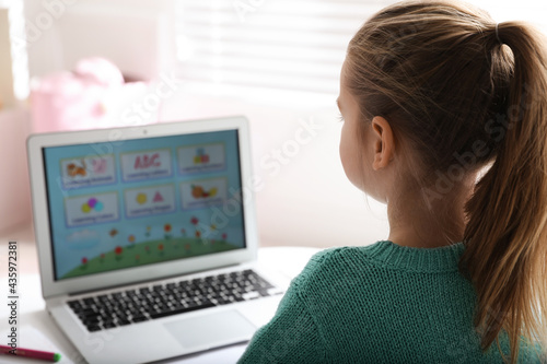 Little girl learning English indoors at online lesson, back view
