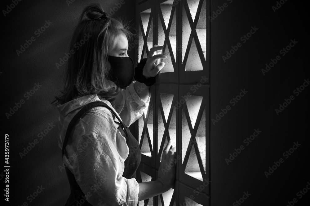 Sad portrait of young scared and worried Asian Thai woman in protective mask standing on stairs at home lockdown and quarantine during covid-19 virus pandemic in dramatic light