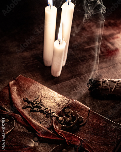 Old antique book with candle and burning smoky incense in vintage style on wooden table. Mystical concept. © roman