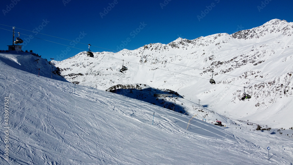 Ski lift in Galtür with white mountains and ski slopes. This shot was taken in the winter with a clear, blue and sunny sky. 