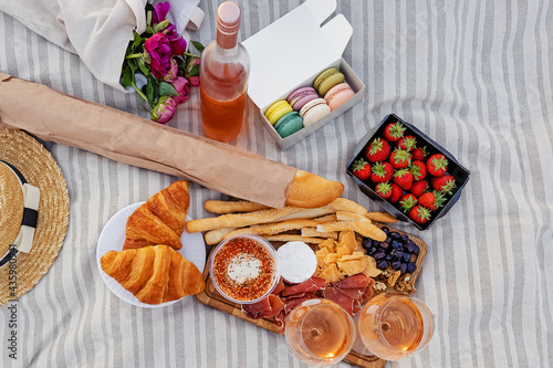 Picnic with strawberries, croissants and appetizers on the board and rose wine