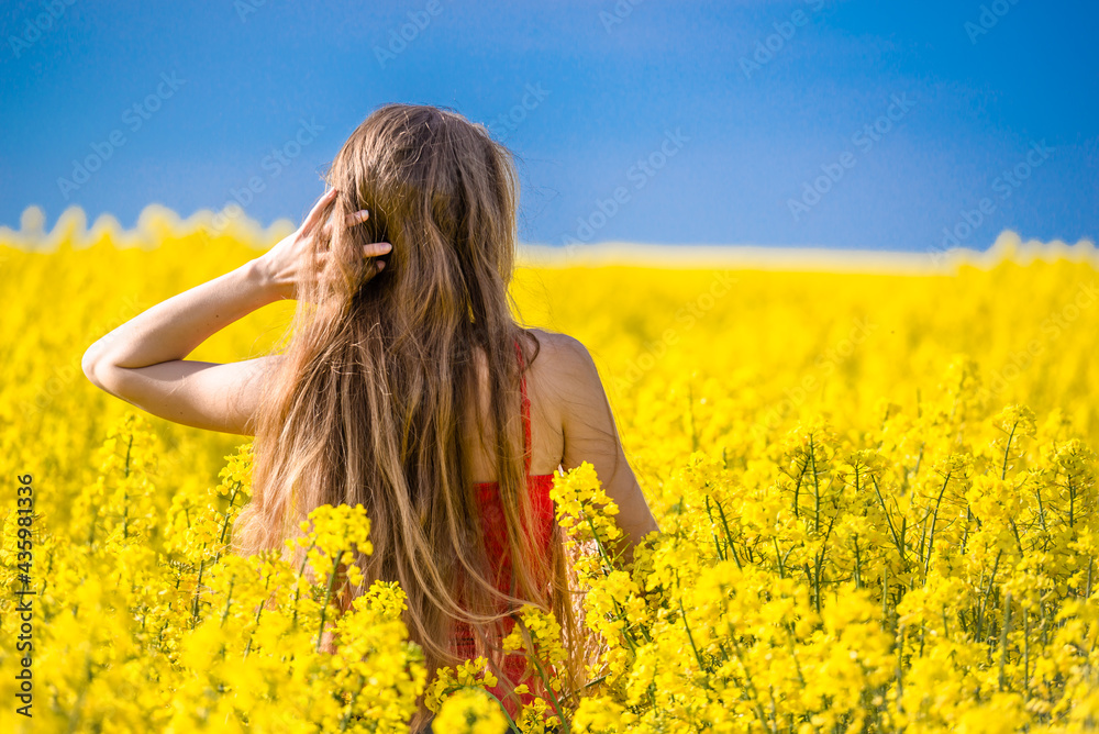 Happy woman in rapeseed field at spring. Back view of a young girl enjoying sun in blooming field. Freedom concept.