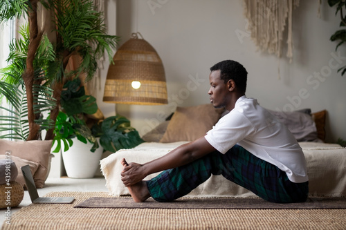 African young man sitting in paschimottanasana or Intense Dorsal Stretch pose, seated forward bend posture photo