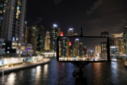 DUBAI, UNITED ARAB EMIRATES - NOVEMBER 03, 2018: Night cityscape of marina district, blurred view. Taking photo with smartphone mounted on tripod © New Africa