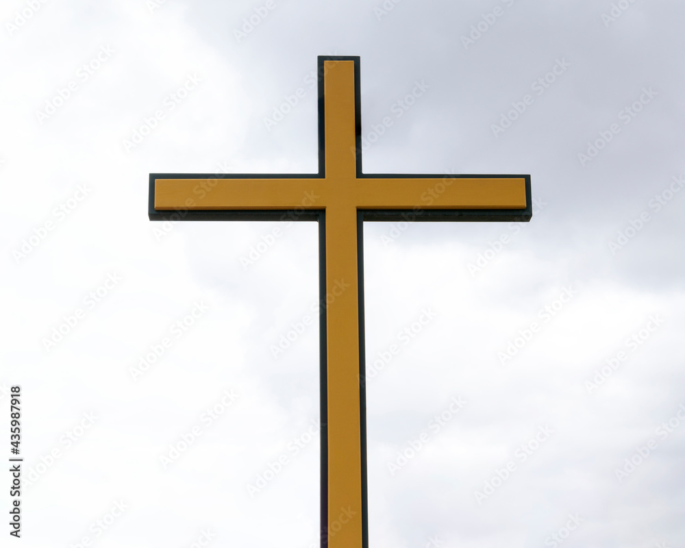 Christian Catholic cross. Color - yellow with black edging. Background - the sky with clouds. Catholic religious symbol concept.