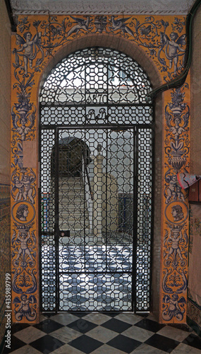 the entrance of a traditional house with a metal barred door with colorful tiles on the walls, in Cadiz, Spain