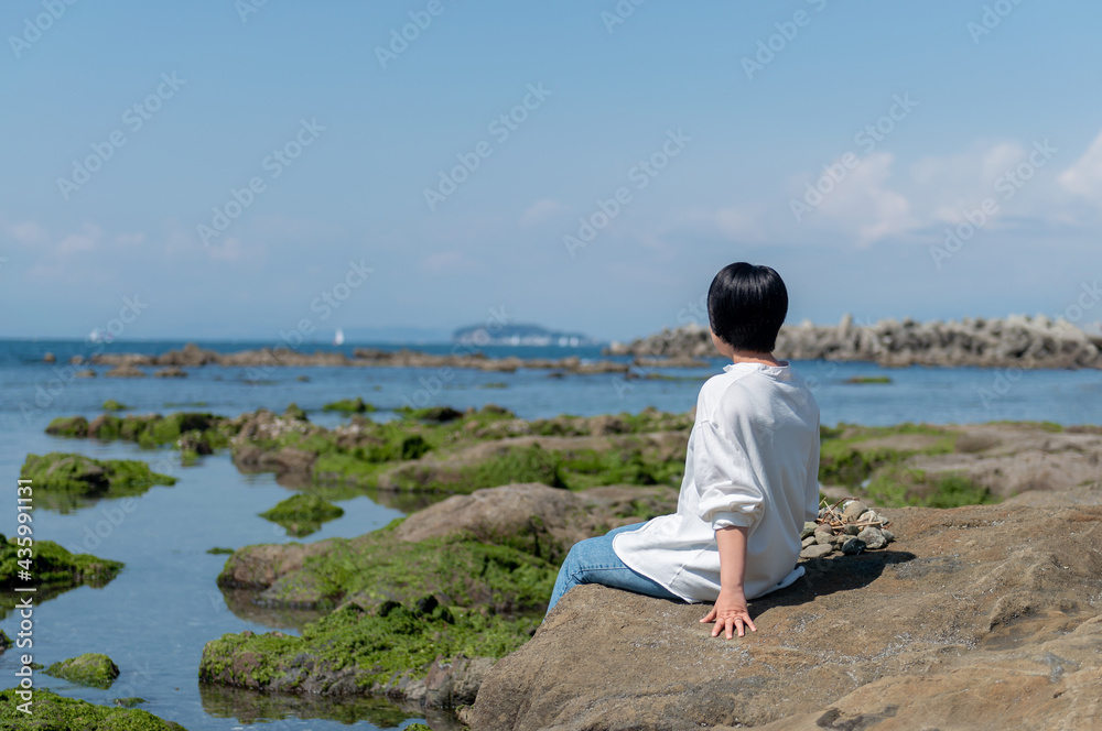 岩場に座って海を眺めながらくつろぐ女性 岩場に座って海を眺めながらくつろぐ女性