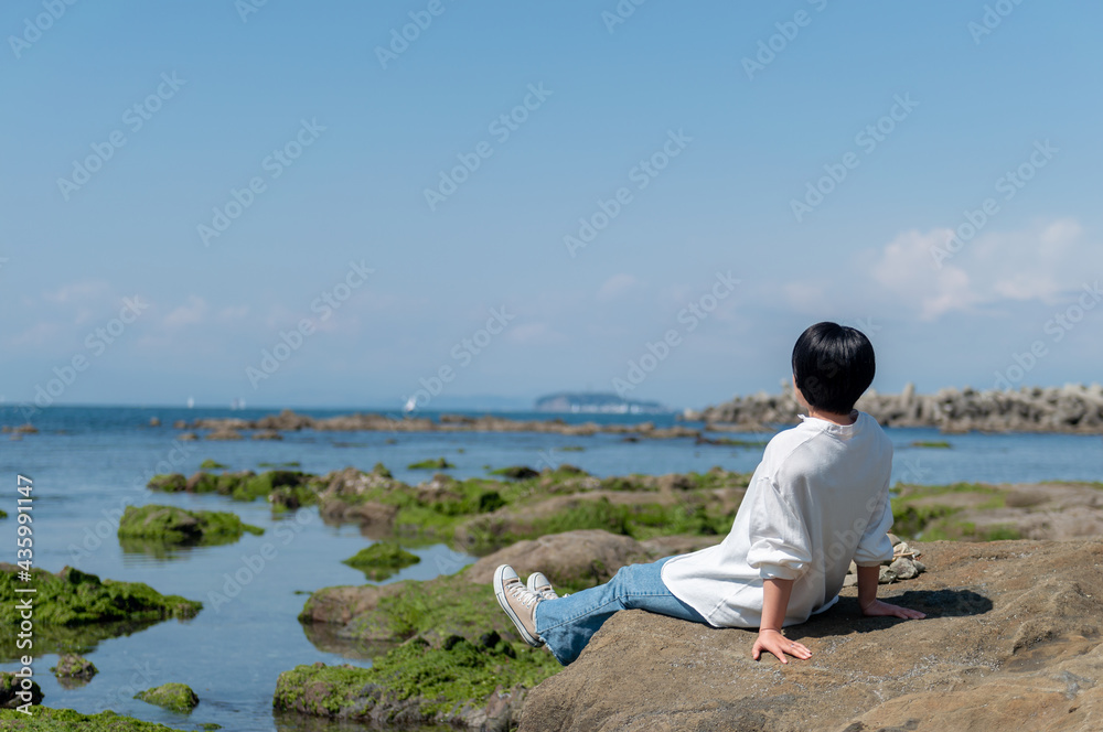 岩場に座って海を眺めながらくつろぐ女性