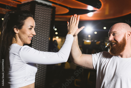 Coach and athletic girl hit hands and give high five at sports club after successful fitness and bodybuilding workout