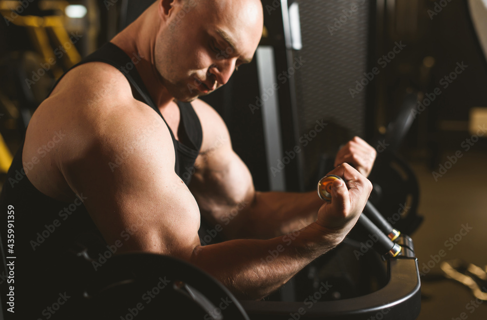 A male bodybuilder performs a biceps exercise in a sports club. The athlete is preparing for the competition. A male bodybuilder performs a biceps exercise in a sports club. The athlete is preparing for the competition.