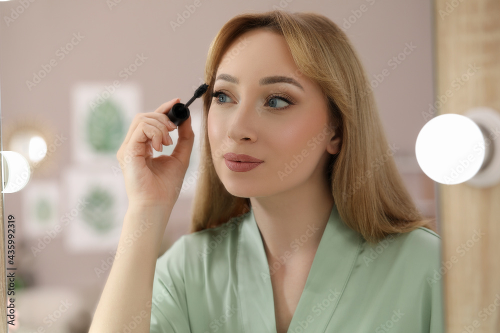 Reflection of beautiful young woman applying mascara in mirror at home Reflection of beautiful young woman applying mascara in mirror at home
