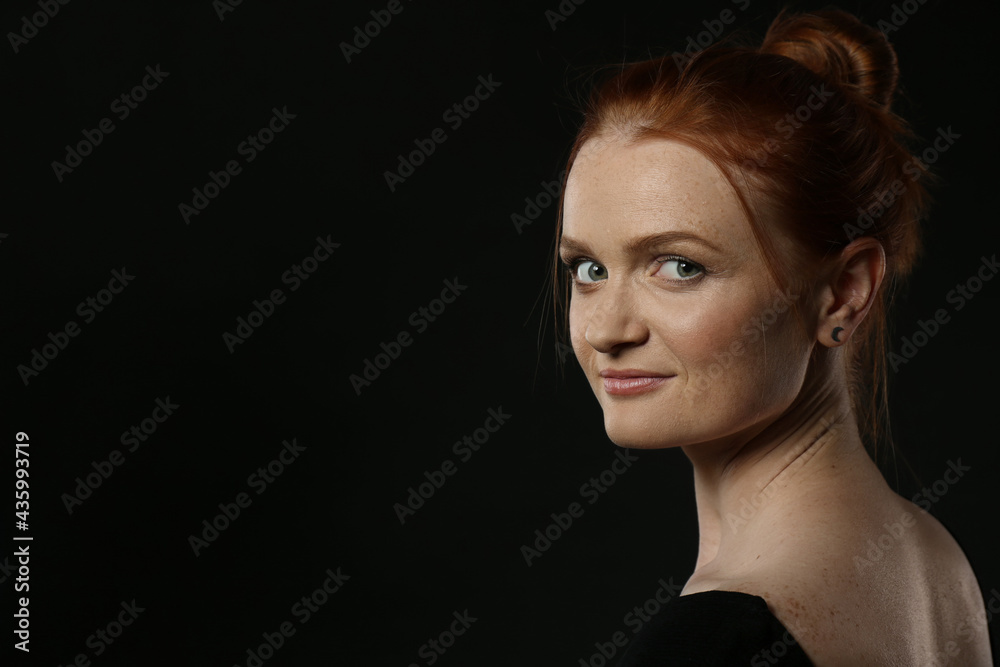 Candid portrait of happy red haired woman with charming smile on dark background, space for text Candid portrait of happy red haired woman with charming smile on dark background, space for text