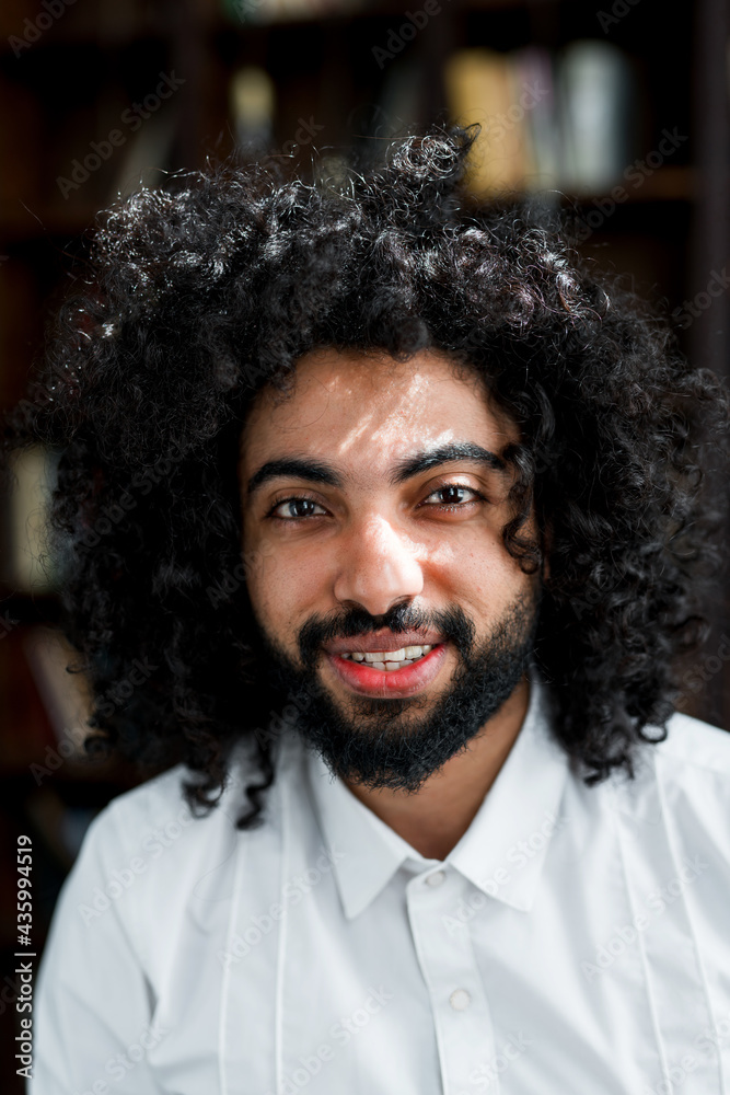 Portrait of happy african american man with beard and afro hairstyle smiling on background of books Portrait of happy african american man with beard and afro hairstyle smiling on background of books