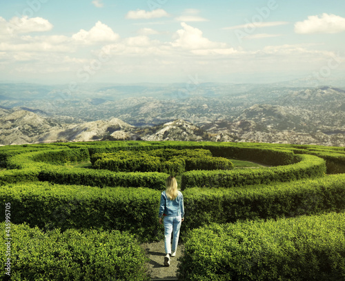 Young woman in hedge maze on sunny day, back view