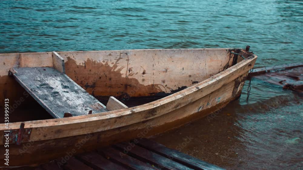 An old makeshift boat made of wood bobs on the waves. It slams its starboard side against the wooden scaffolding. The boat has two seats for passengers. The video is slow-motion. An old makeshift boat made of wood bobs on the waves. It slams its starboard side against the wooden scaffolding. The boat has two seats for passengers. The video is slow-motion.