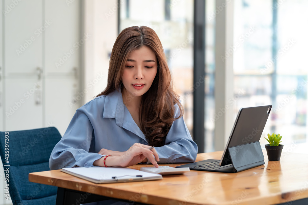 Asian businesswoman calculating financial documents using calculator at the office. Asian businesswoman calculating financial documents using calculator at the office.