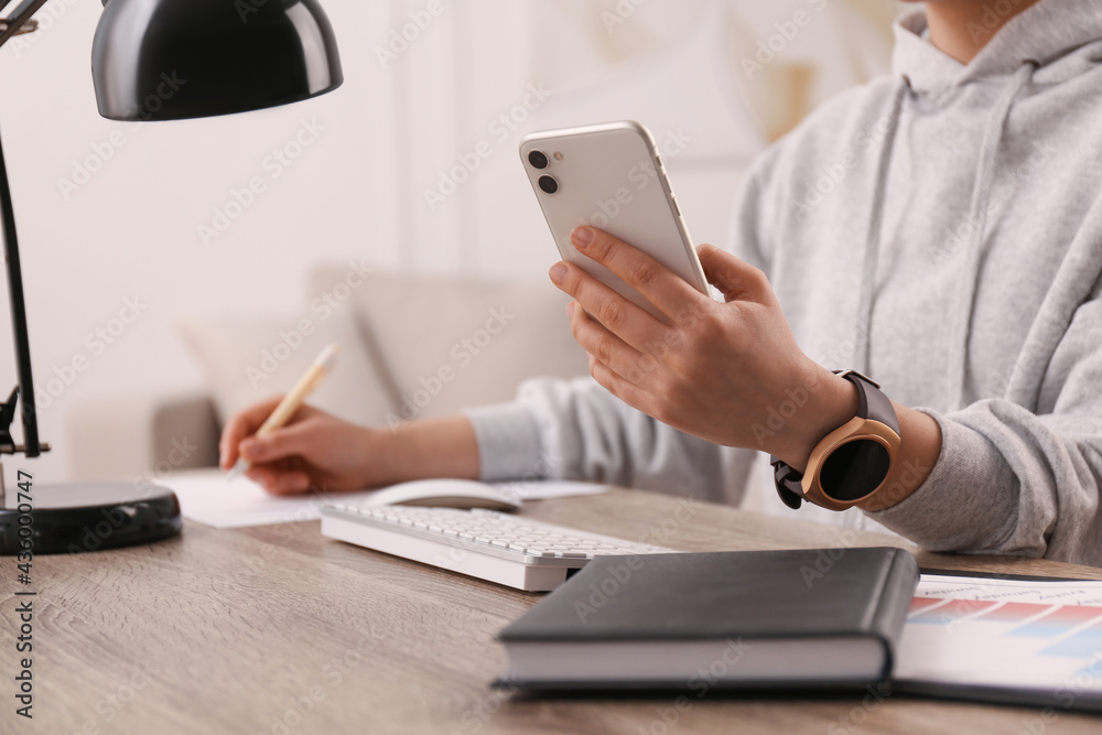 Fototapeta premium Young woman with smart watch and phone at table in office, closeup