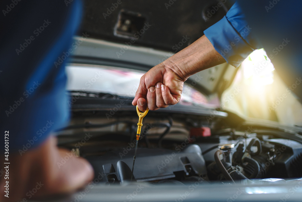 Close up of the hand of an asian mechanic. Auto mechanic is checking the engine oil in a vehicle at the garage. Maintenance concept.