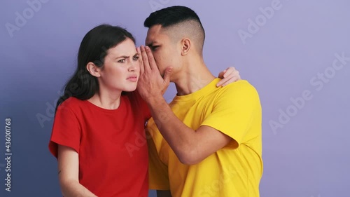 The unpleasantly surprised couple pointing to the camera and whispering something in each other's ear while standing in the studio