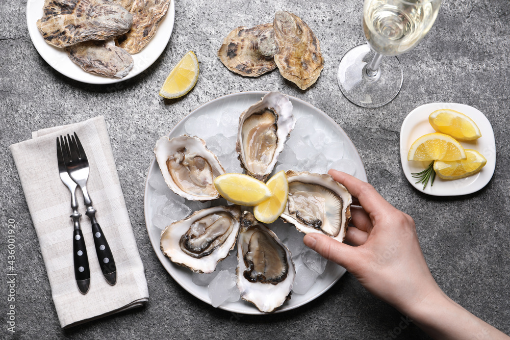 Woman eating tasty fresh oysters at grey table, top view